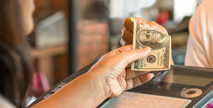 Customer handing an older design $100 bill to cashier at the cash register.